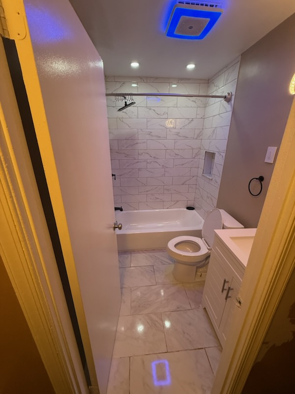Renovated guest bathroom with tiled tub surround, accent niche and white vanity